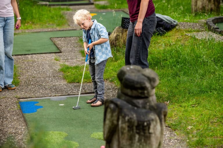 Jong kind slaat de midgetgolfbal bij De Rheezerbelten terwijl een volwassene toekijkt