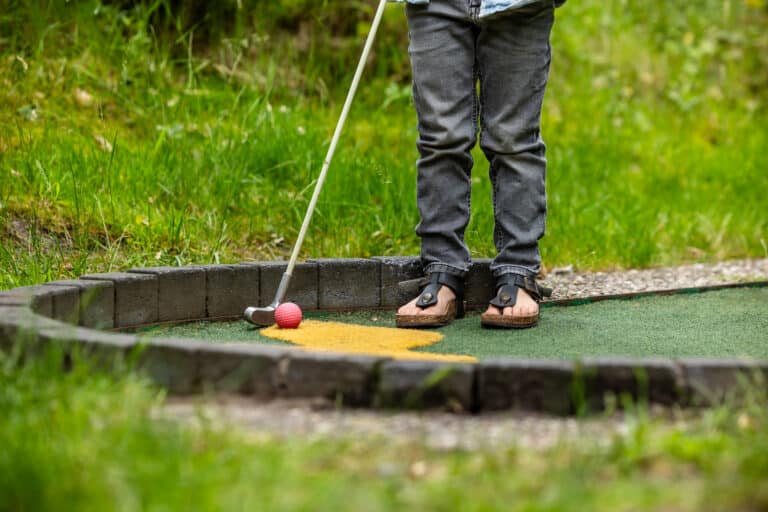 Iemand staat klaar om een rode midgetgolfbal te slaan op de baan bij De Rheezerbelten
