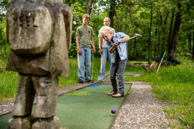Oudere jongen slaat een paarse midgetgolfbal op de buitenbaan bij De Rheezerbelten