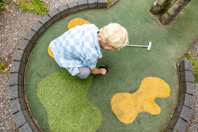 Jong kind pakt de midgetgolfbal op uit de hole, close-up op de baan bij De Rheezerbelten