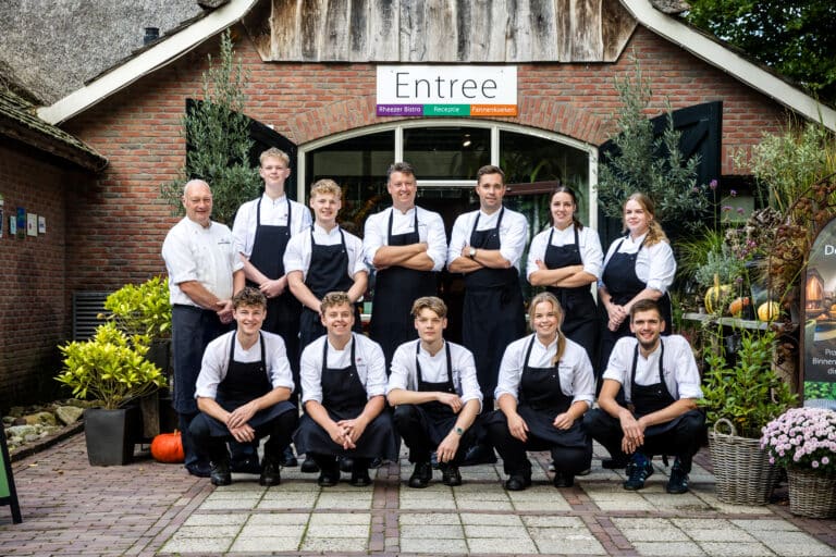 Teamfoto van De Rheezerbelten voor het entreegebouw met bord